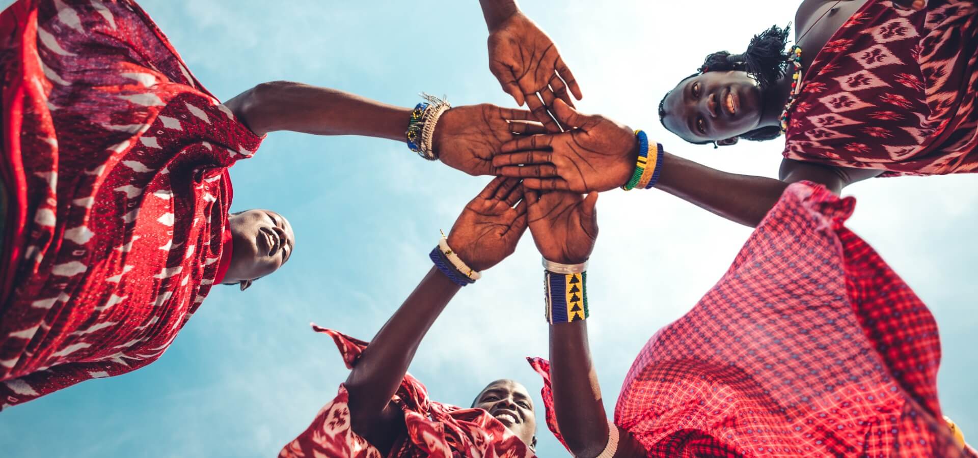 Group of Black women joining their hands together, Grupo de mujeres afrodescendientes uniendo las manos, low-angle shot with the sky in the background.