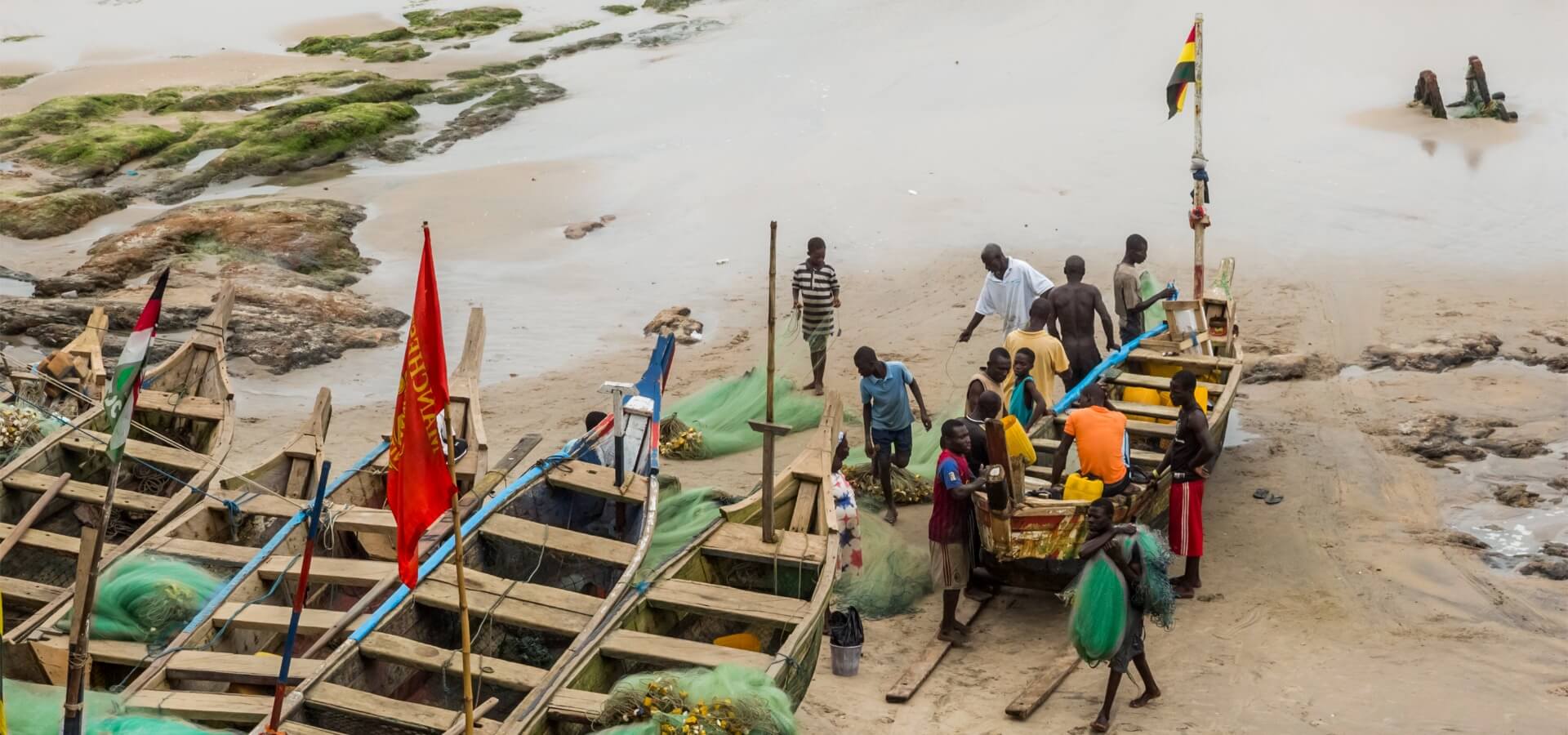 Group of Black fishermen next to two boats in the sand.