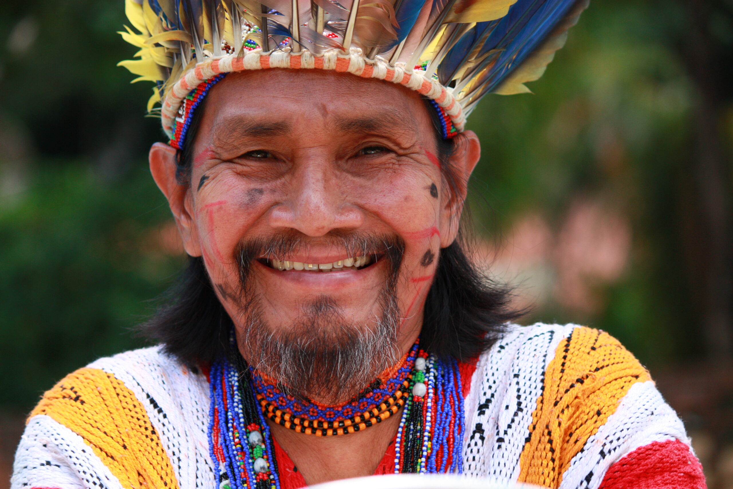 Portait Indigenous Katukina is standing in the middle of bushes, his face  painted with urucum and he wears ethinic clothing.